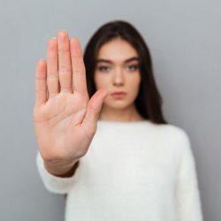Close up portrait of a woman showing stop gesture with her palm isolated over gray background